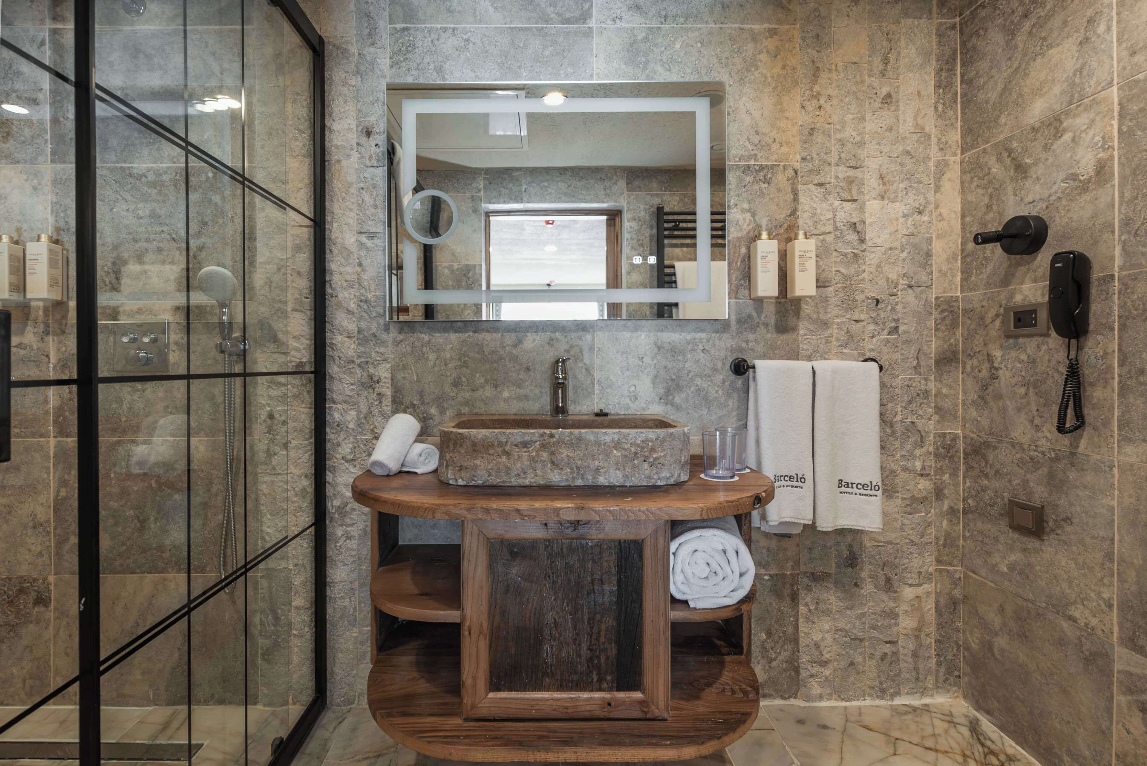A modern bathroom with a stone sink, a large mirror, a glass shower enclosure, and a wooden vanity.