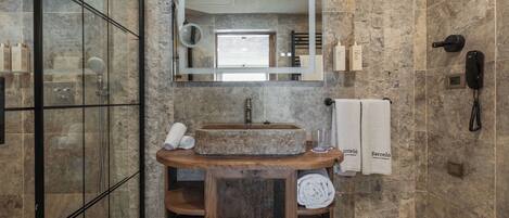 A modern bathroom with a stone sink, a large mirror, a glass shower enclosure, and a wooden vanity.