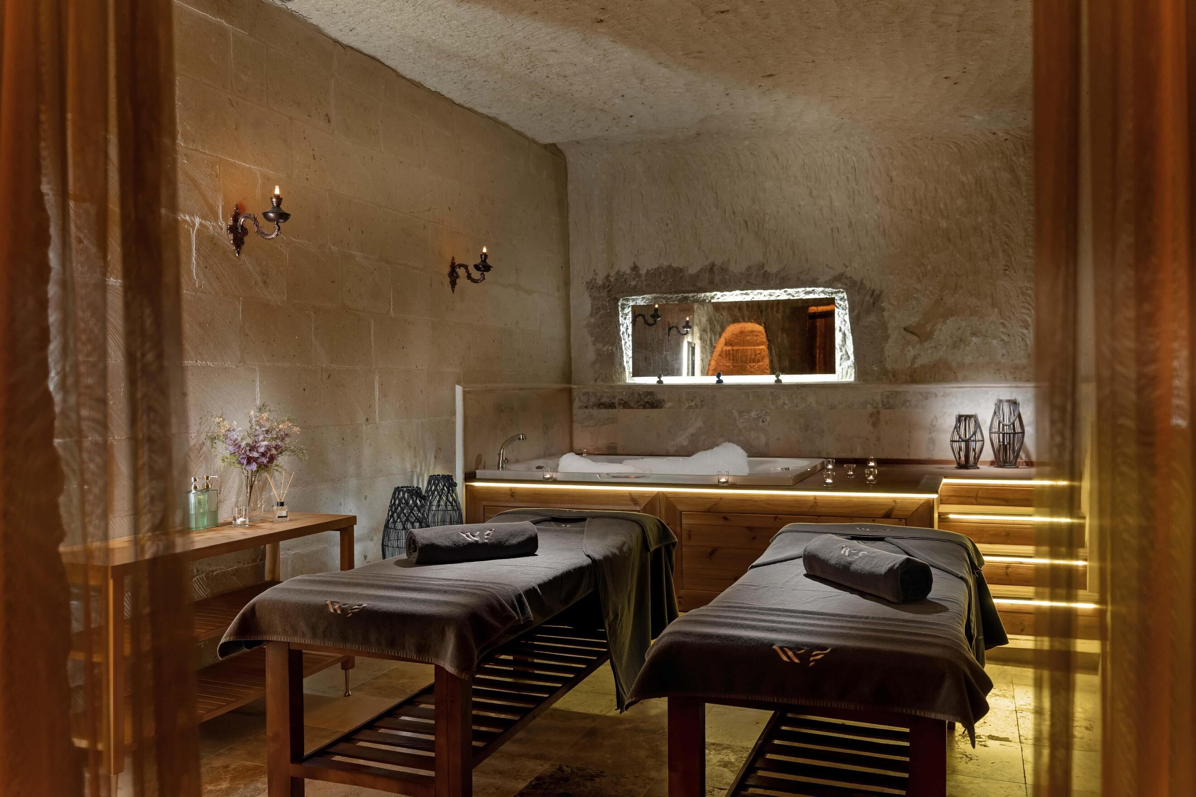 Un cuarto de spa con dos camillas de masaje, un banco de madera, un lavamanos y un espejo.
