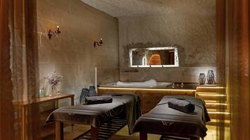 Un cuarto de spa con dos camillas de masaje, un banco de madera, un lavamanos y un espejo.