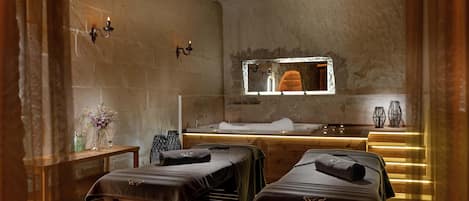 A spa room with two massage tables, a wooden bench, a sink, and a mirror.
