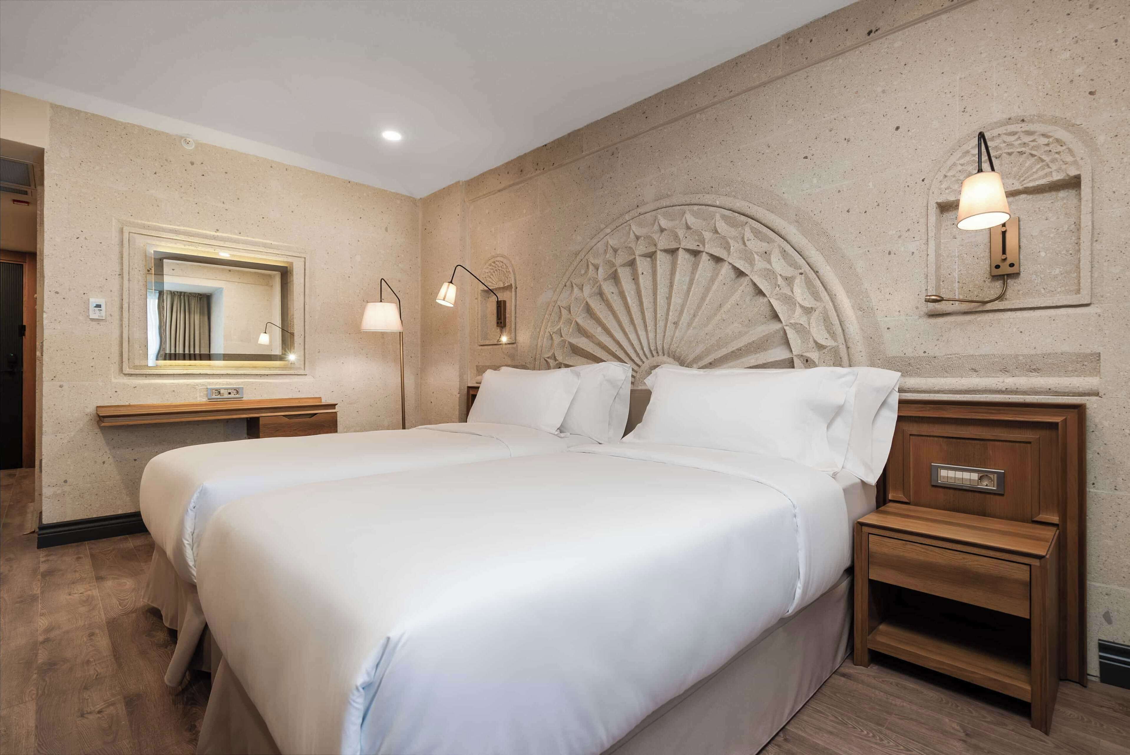 A hotel room with a large bed, two bedside tables, a wall-mounted mirror, and a decorative headboard.
