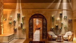 Um lobby luxuoso com uma porta arqueada central, área de estar com cadeiras e plantas decorativas nas paredes.
