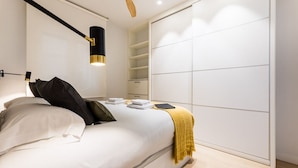 A modern bedroom with a bed, bedside tables, a wardrobe, and a ceiling light fixture. - SUNRISE BEACH APARTMENT by Sweet Home (San Sebastián)