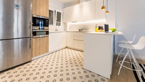 A modern kitchen with stainless steel appliances, wooden cabinets, and a white island with bar stools. - SUNRISE BEACH APARTMENT by Sweet Home (San Sebastián)