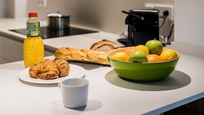 A modern kitchen with a white countertop, a green bowl of fruit, a croissant, a coffee cup, and a bottle of juice. - SUNRISE BEACH APARTMENT by Sweet Home (San Sebastián)