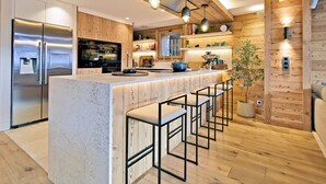 Une cuisine moderne dotée d’un îlot central, de tabourets de bar, d’éléments décoratifs en bois et d’appareils électroménagers intégrés.