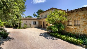 A two-story stone building with a gravel driveway, surrounded by greenery and trees. - Beautiful villa with stunning view nestled in countryside near Valbonne village  (OPIO)