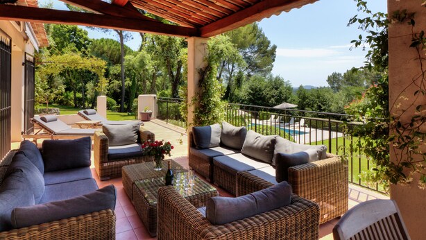 A covered outdoor seating area with wicker furniture, a pool, and a view of the surrounding greenery. - Beautiful villa with stunning view nestled in countryside near Valbonne village  (OPIO)