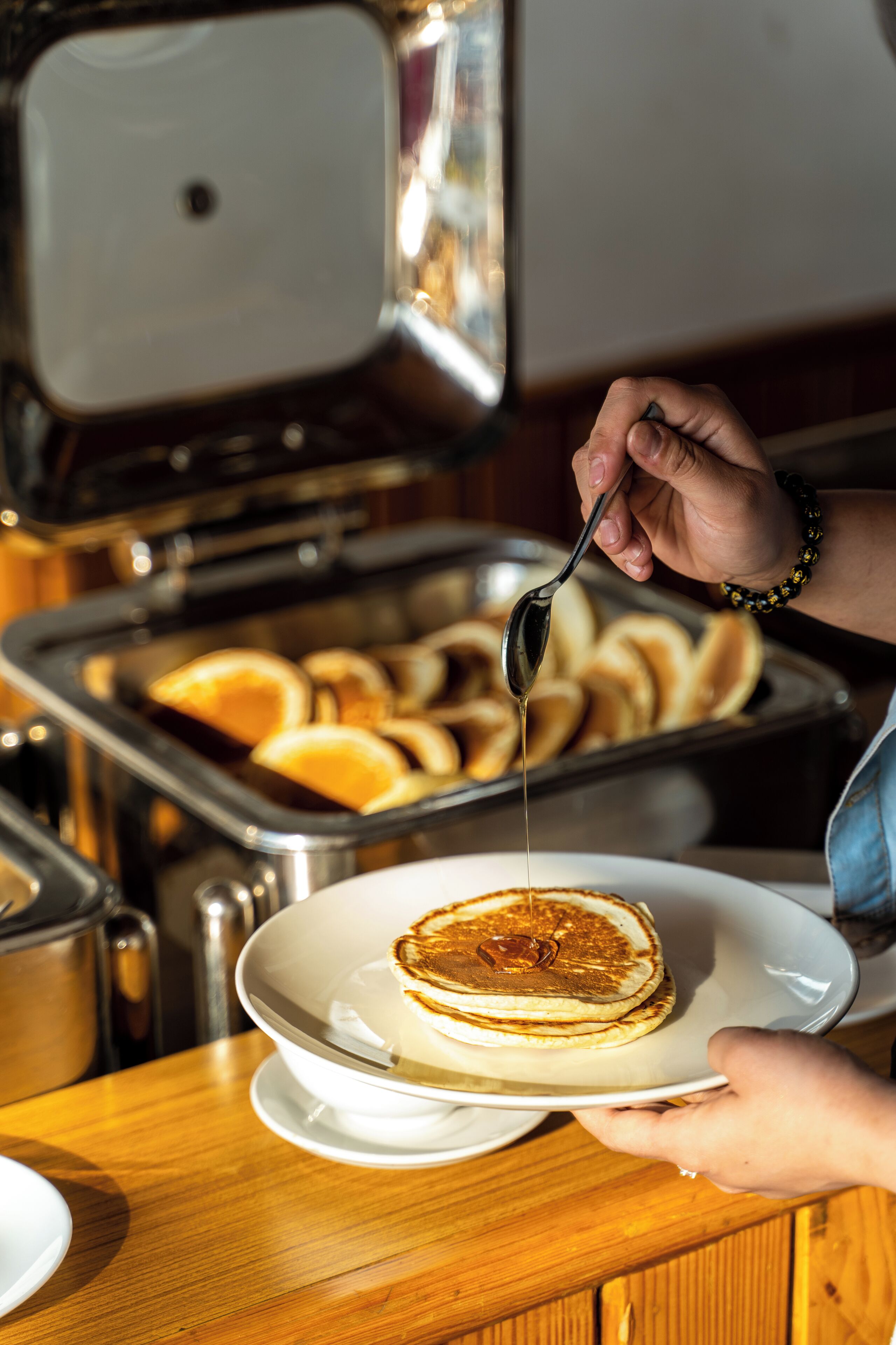 A person serving pancakes with syrup on a plate.