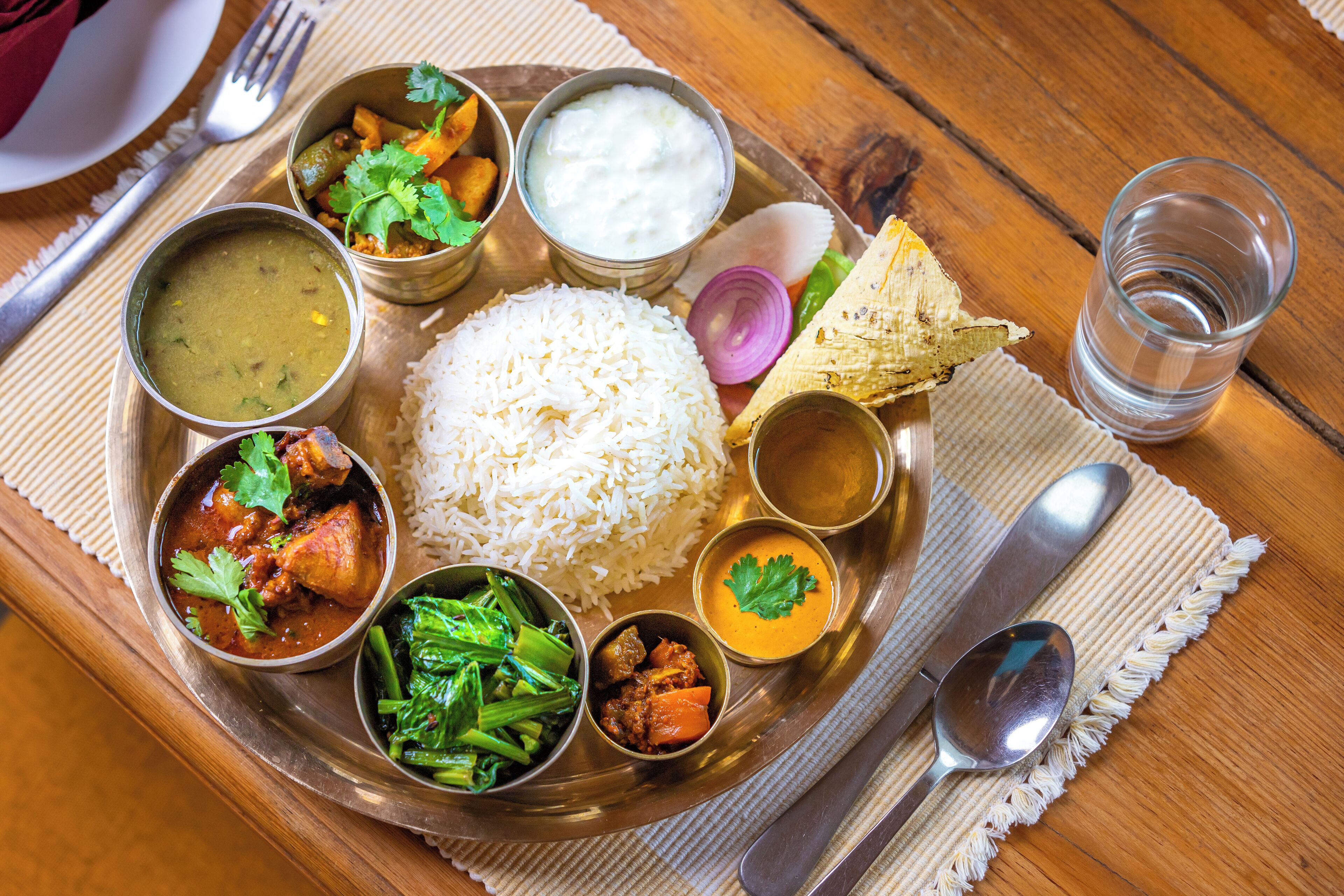 A traditional Indian meal on a metal tray with rice, various curries, and a glass of water.