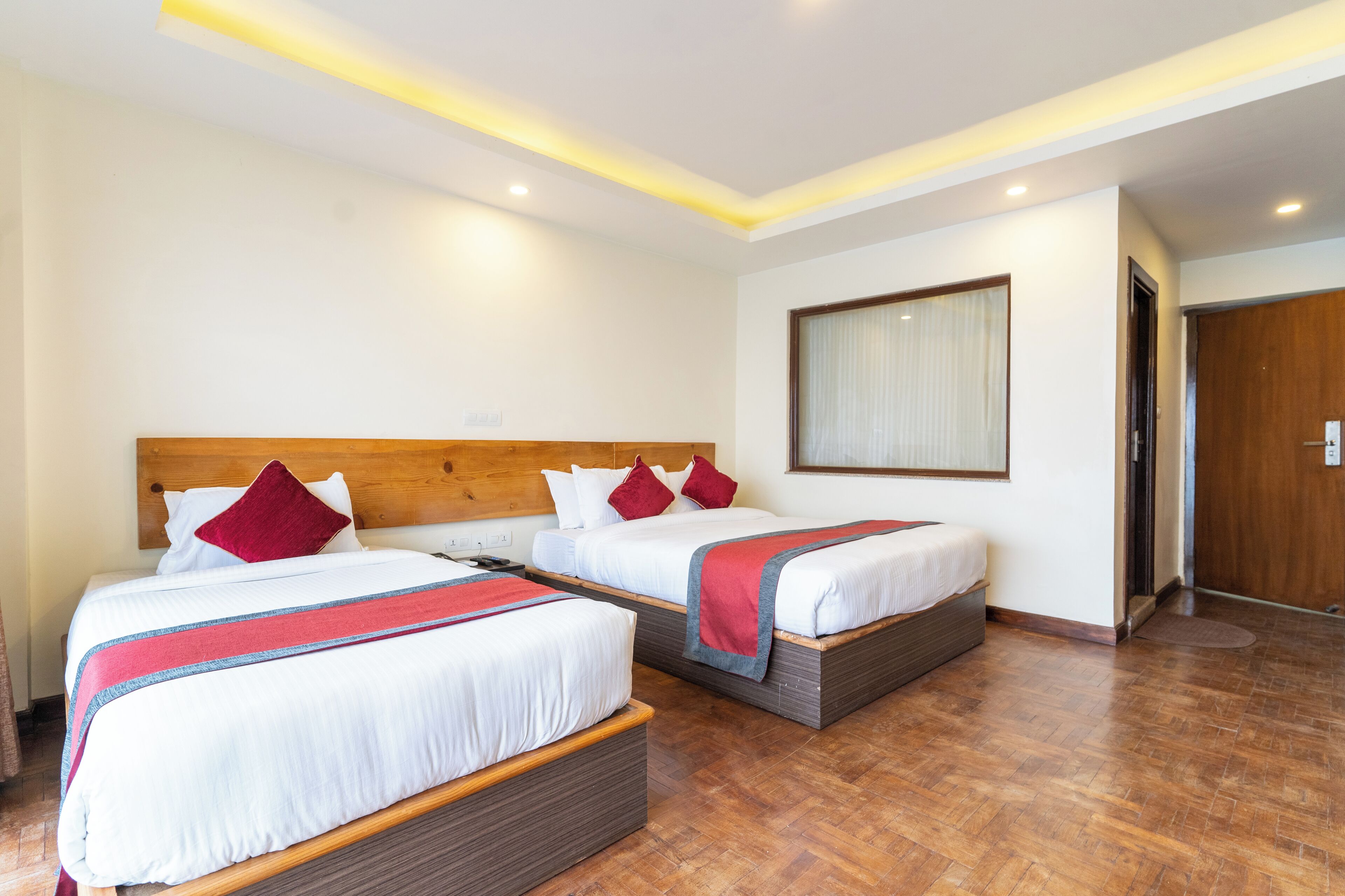 Een hotelkamer met twee bedden, houten hoofdeinden, witte beddengoed en rode kussens, plus een houten deur.