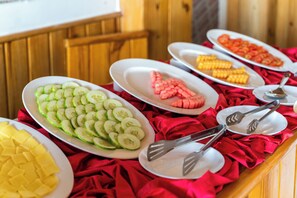 Ein Buffet mit verschiedenen Speisen, darunter Gurkenscheiben, Wassermelone, Mais und Ananas.