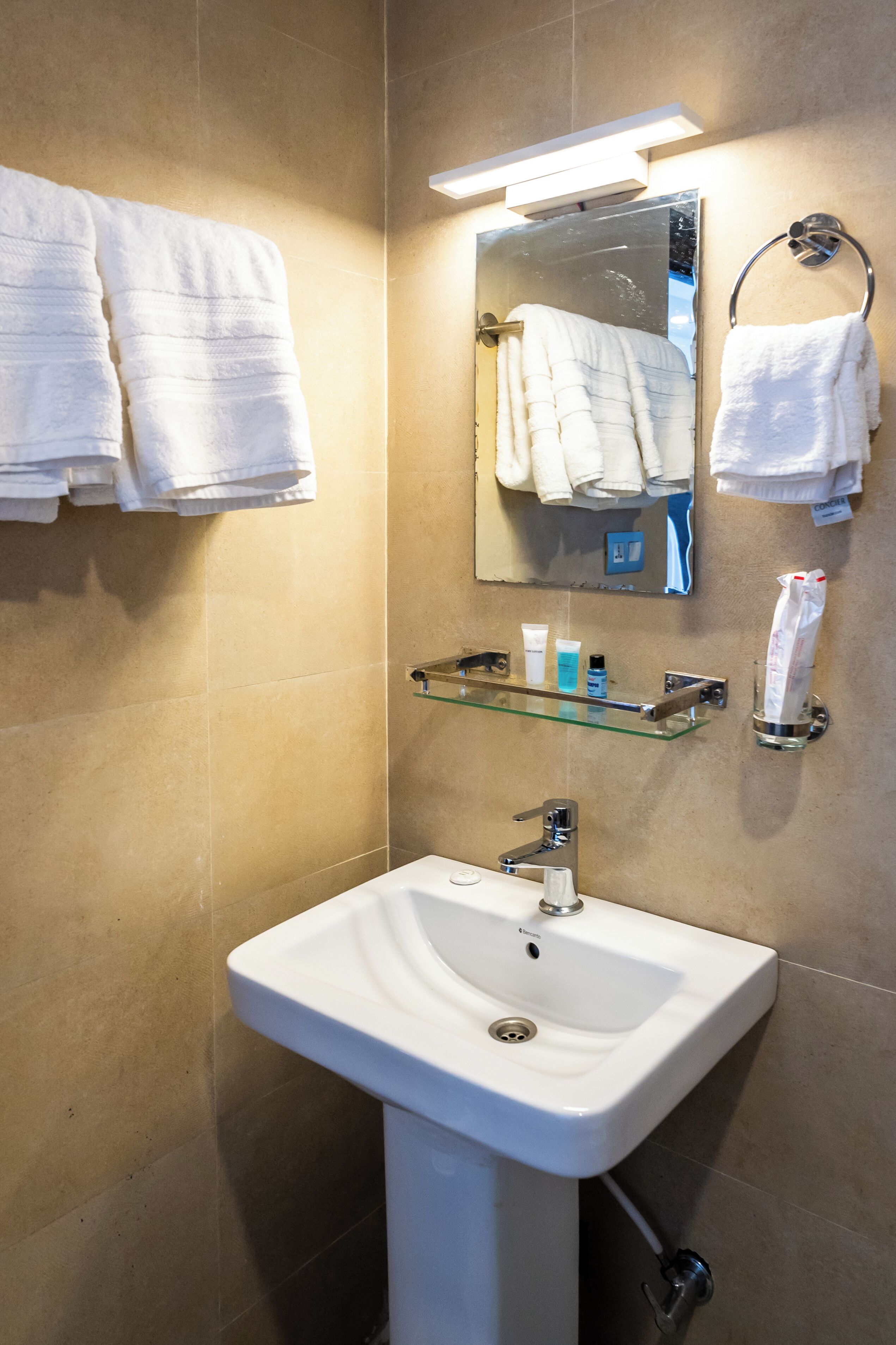 A bathroom with a white sink, a mirror, and multiple white towels hanging on hooks.