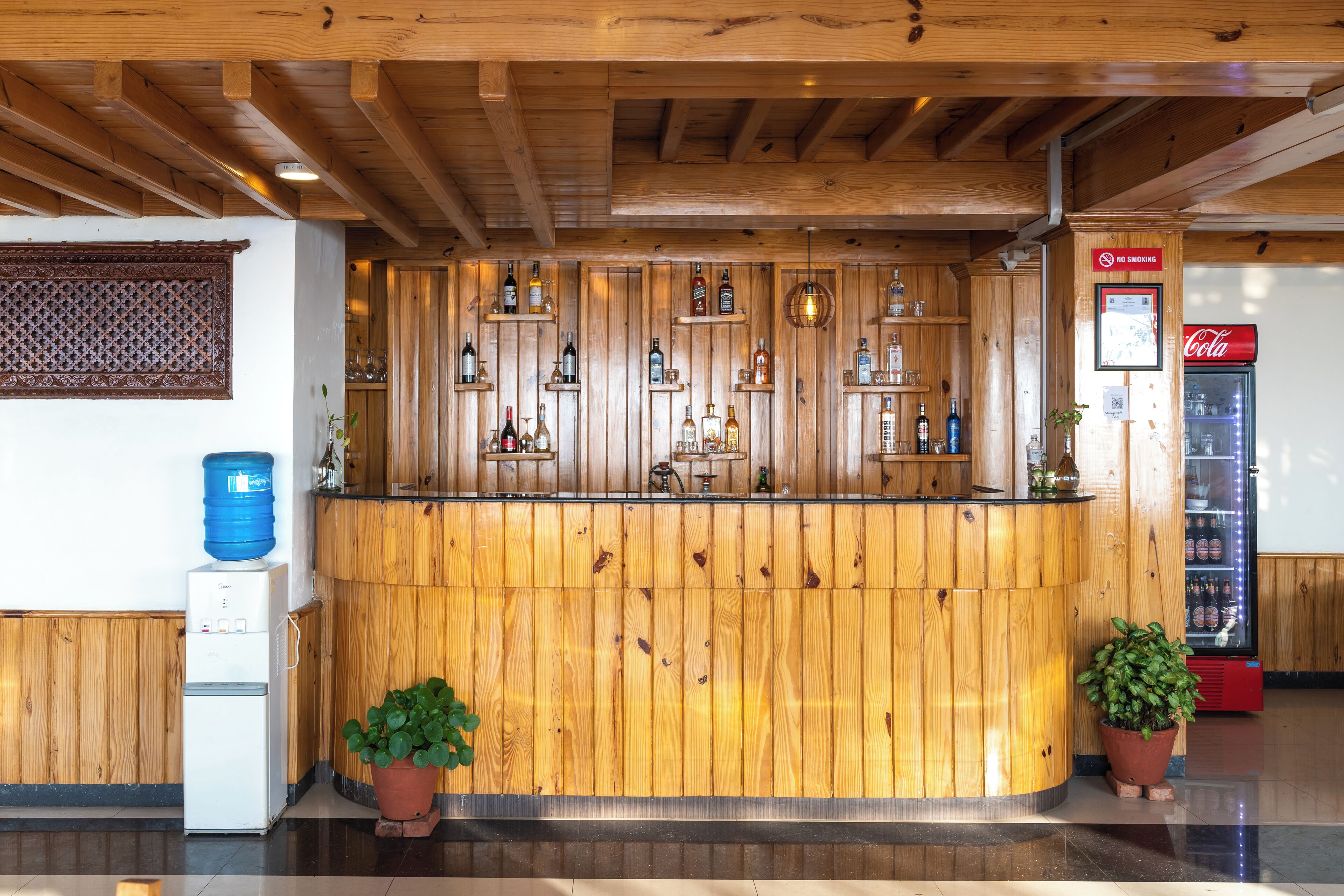 A reception area with a wooden counter, shelves with bottles, a water dispenser, and a Coca-Cola refrigerator.