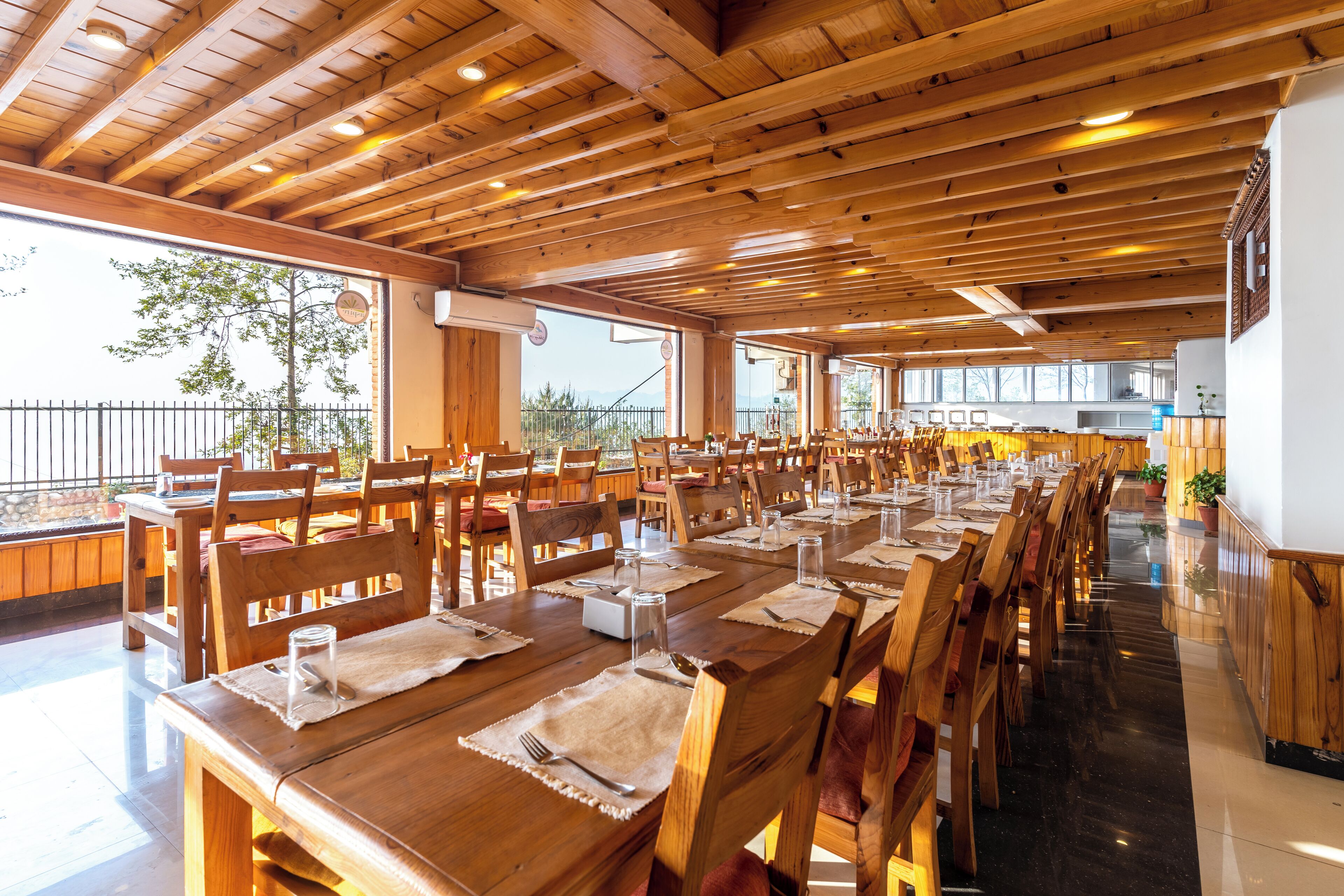 A spacious dining area with wooden tables and chairs, large windows, and a view of the outdoors.