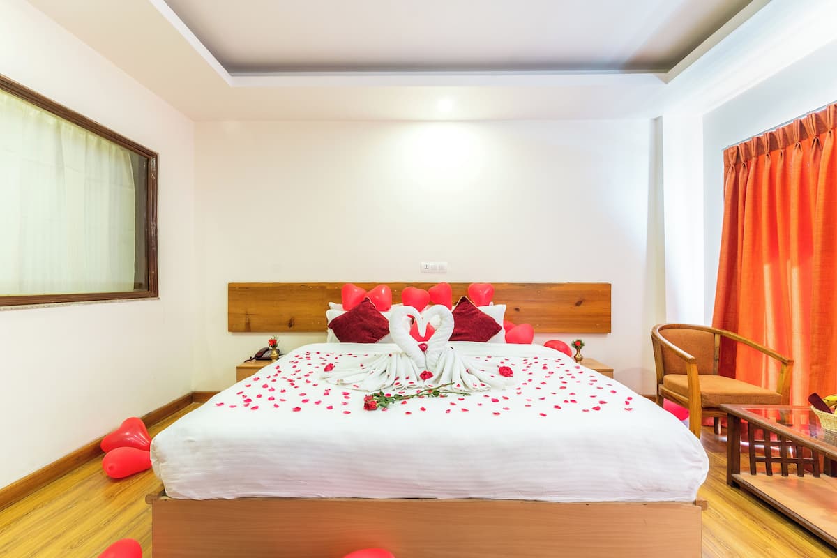 Un lit bien fait, avec un couvre-lit blanc, des oreillers rouges et une décoration en forme de cœur.