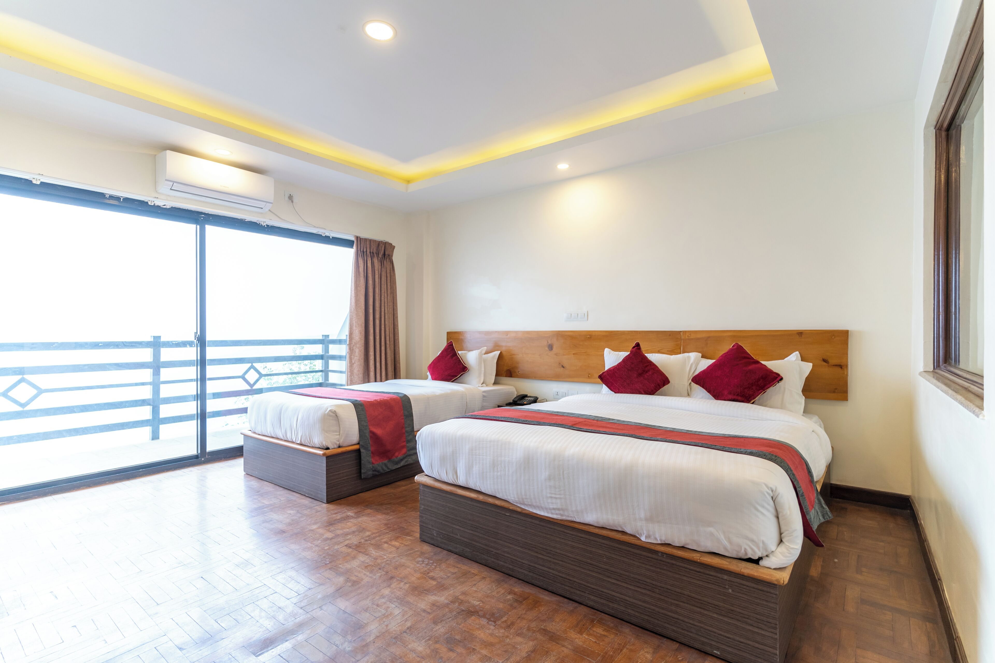 Habitación de hotel con dos camas, cabecera de madera, ventana grande con vistas y unidad de aire acondicionado.