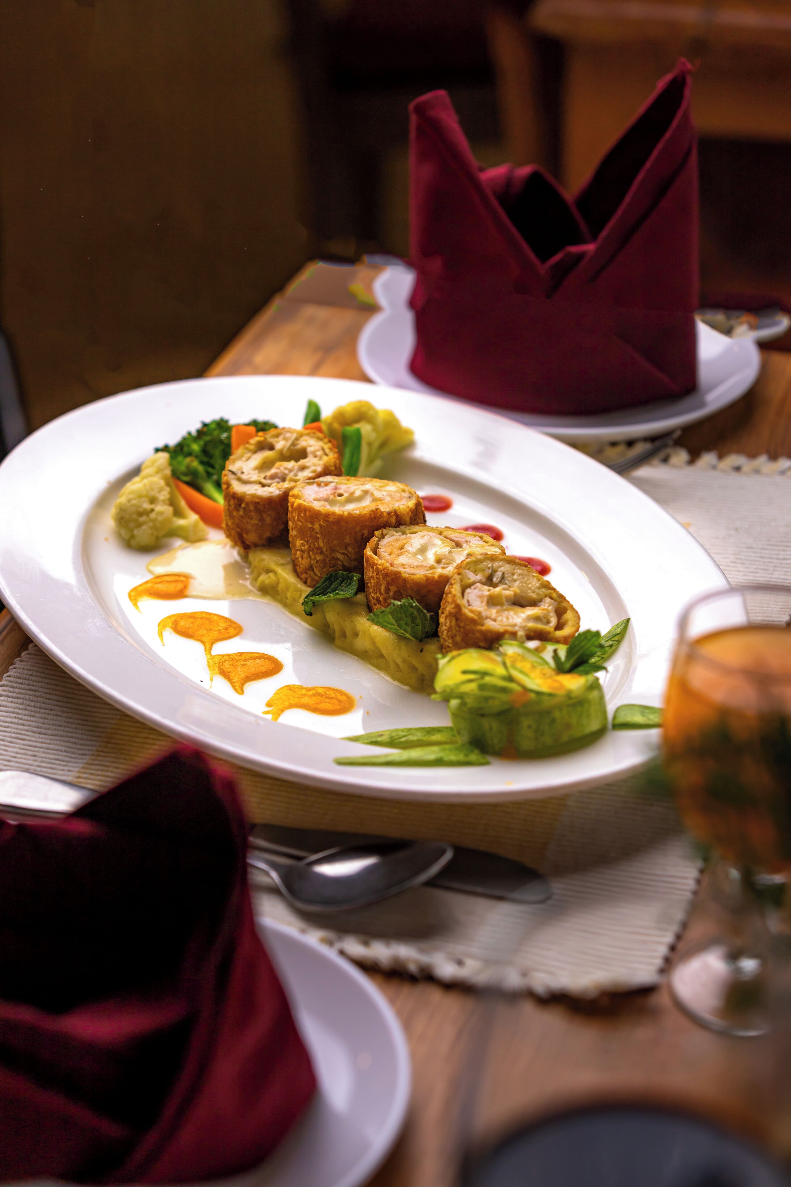 A dining table with a white plate of food, a red napkin, and a glass of beverage.