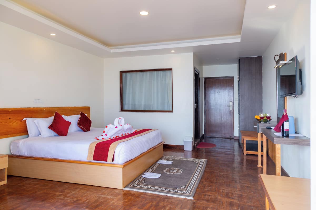 Une chambre d’hôtel avec un lit en bois, un bureau, une chaise, une télévision et une salle de bain visible au fond.