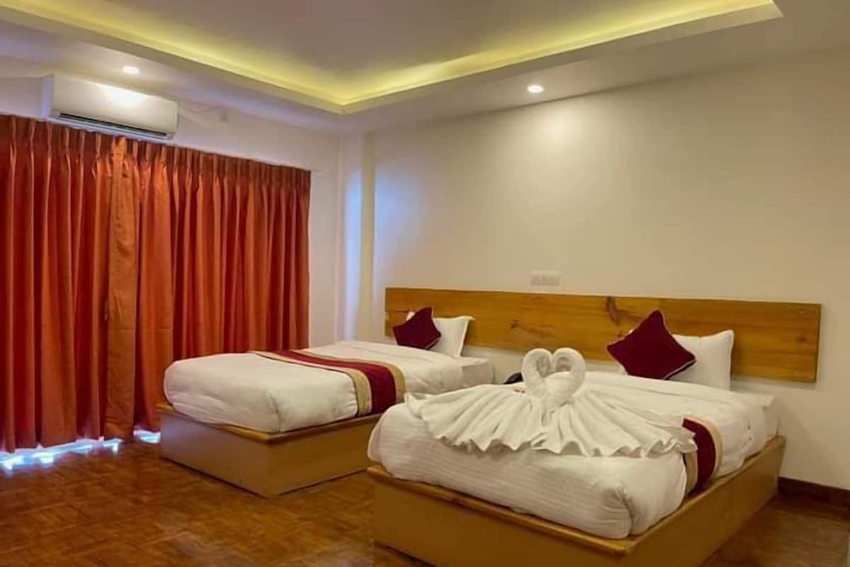 Une chambre d’hôtel avec deux lits, des têtes de lit en bois, des rideaux rouges et un appareil de climatisation.