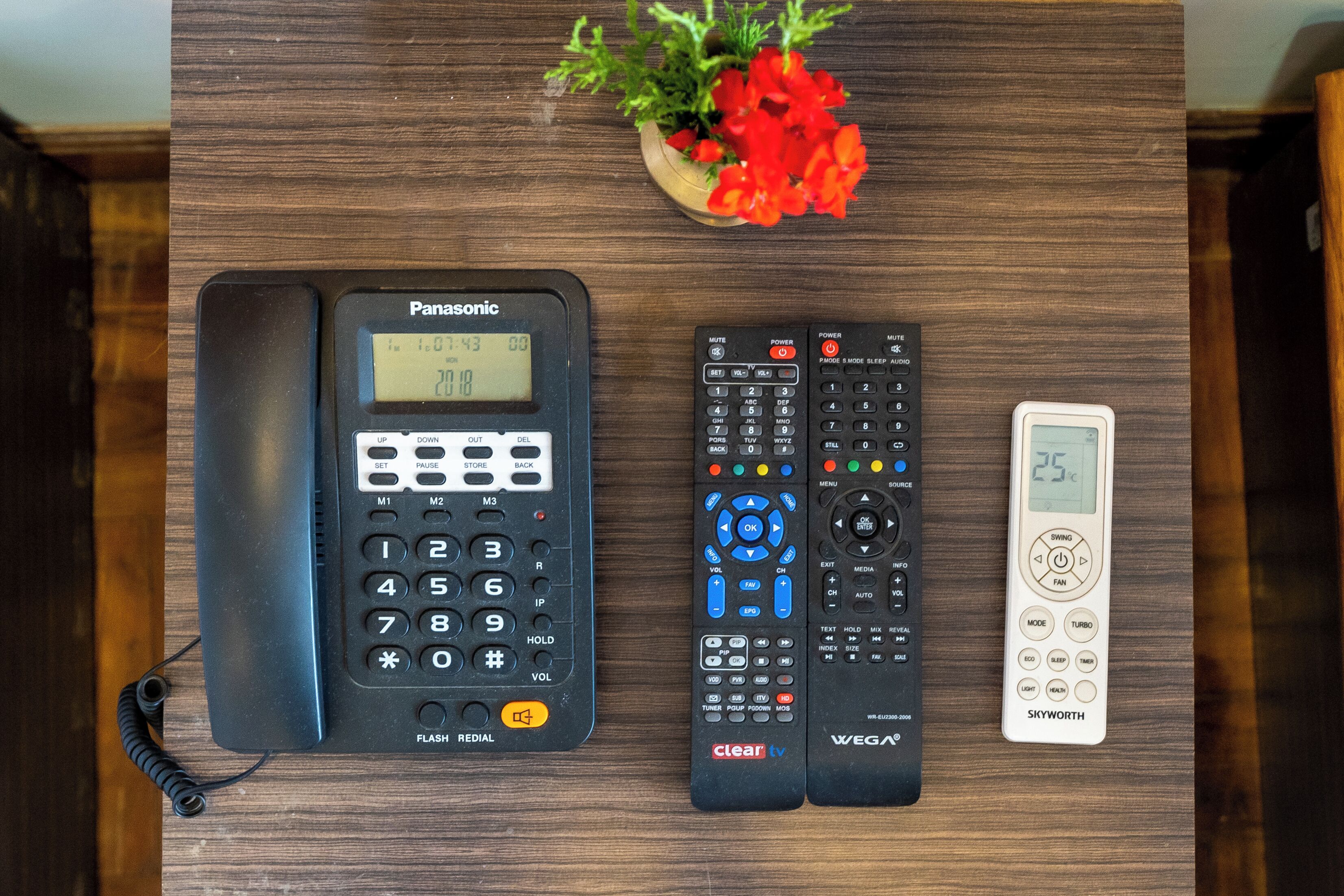 A Panasonic phone, a Clear TV remote, a WEGA remote, and a Skyworth thermometer on a wooden surface.