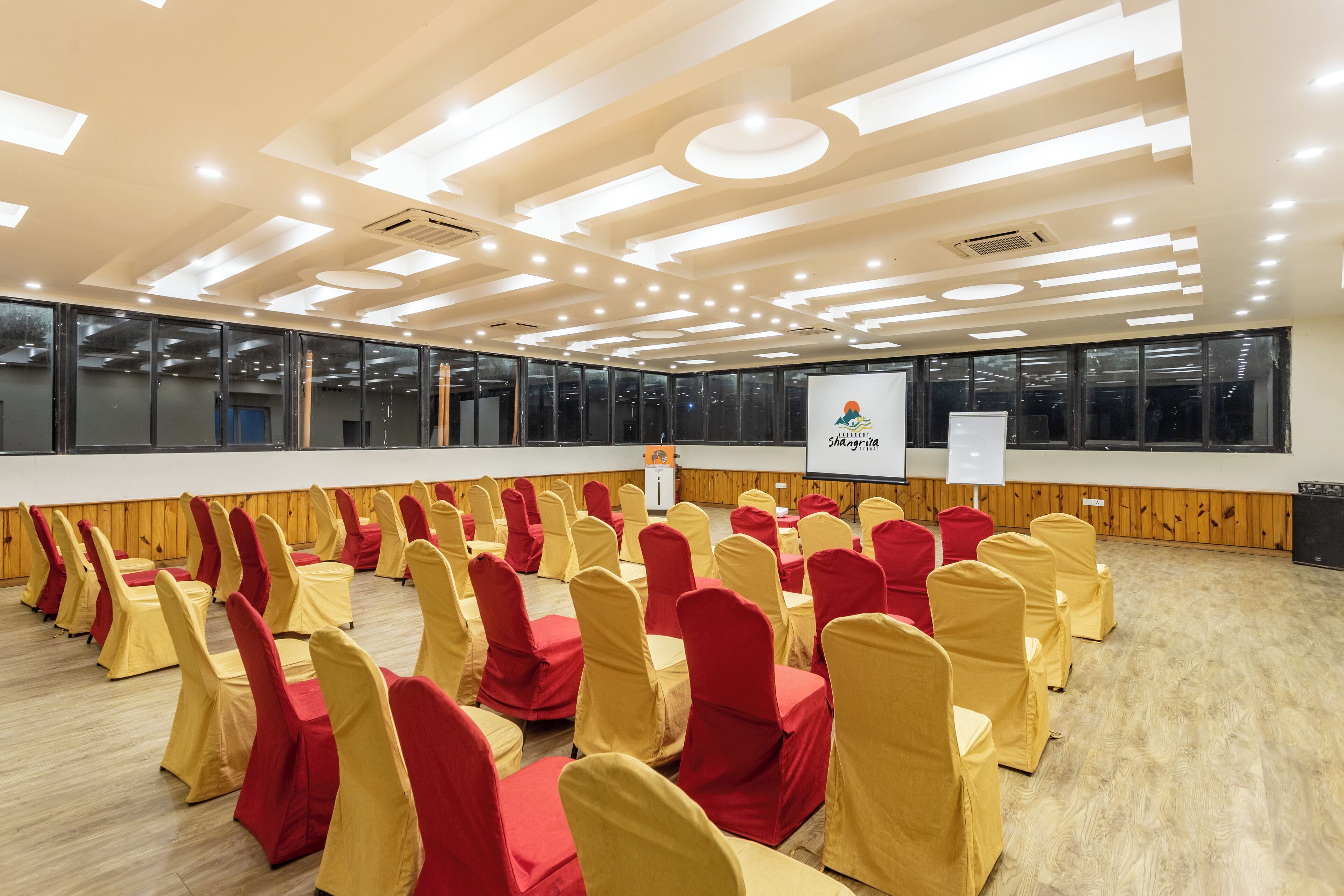 Un salón de conferencias con filas de sillas, un atril y una pantalla para presentaciones.