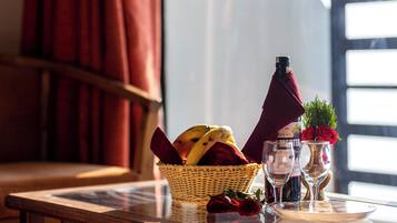 Una mesa con una cesta de mimbre que contiene frutas, una botella de vino, dos copas de vino y un jarrón con una rosa roja.