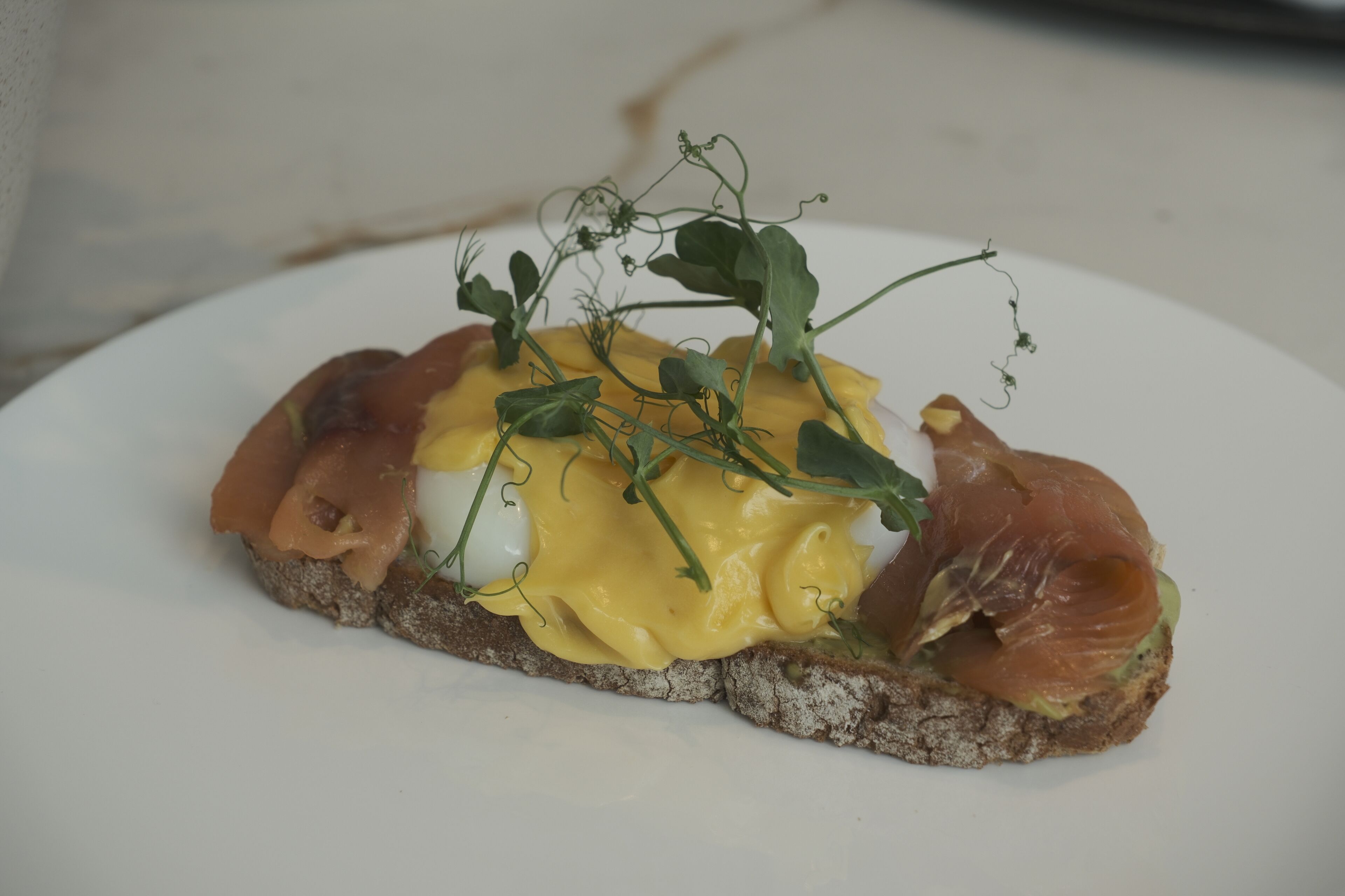 A sandwich with smoked salmon, egg, and greens on a slice of bread.
