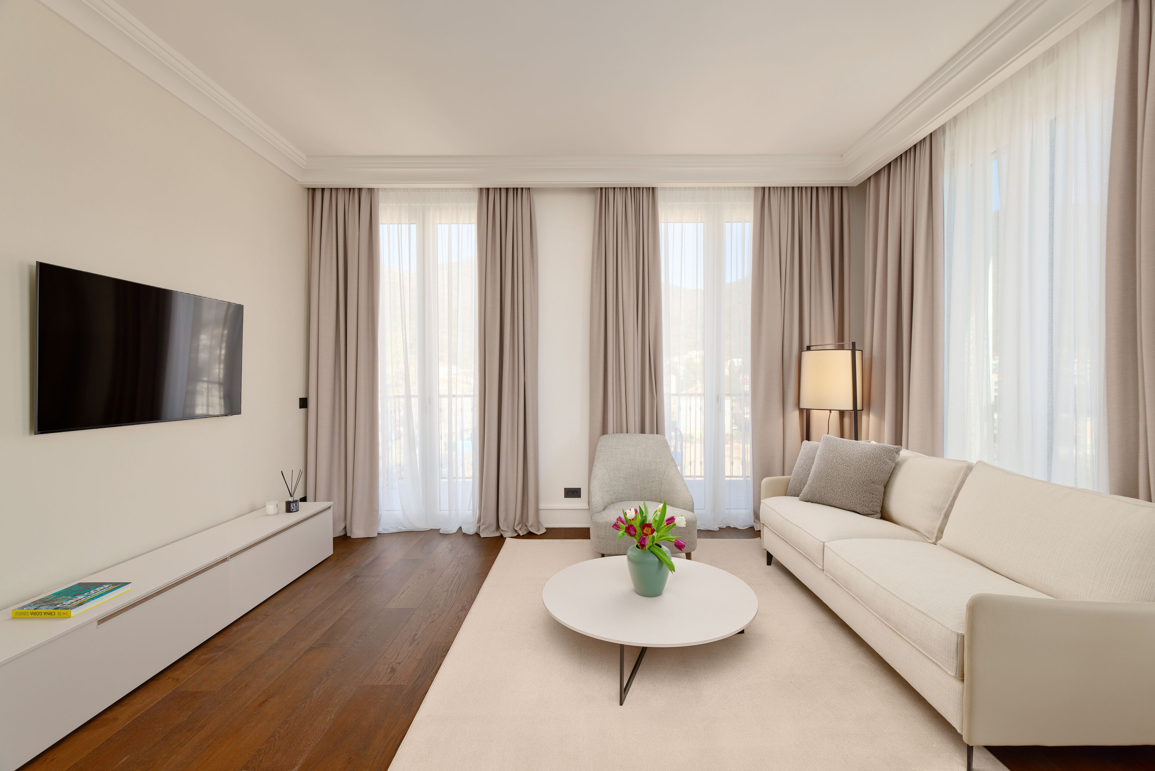 Un salon moderne avec un téléviseur à écran plat, un canapé blanc, une table basse ronde et une lampe.