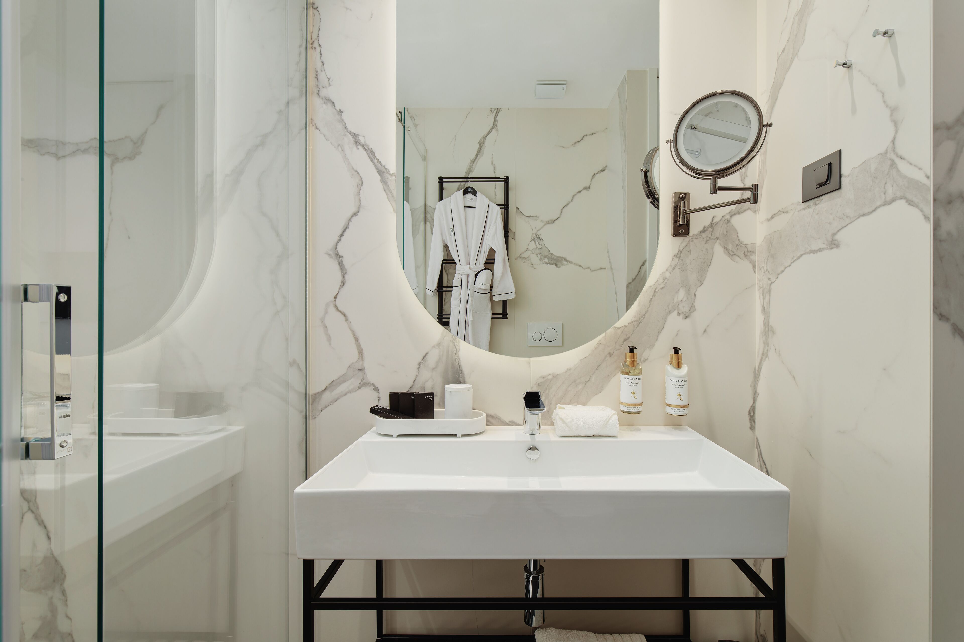 Un baño con lavamanos de mármol blanco, un espejo grande y una cabina de ducha de vidrio.