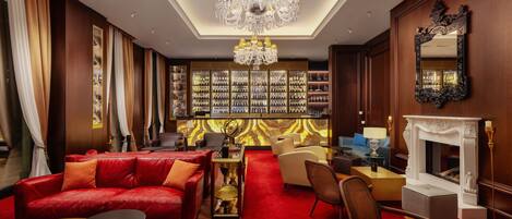 Uma sala de estar luxuosa com um sofá vermelho, lareira, candelabro e estante cheia de livros.