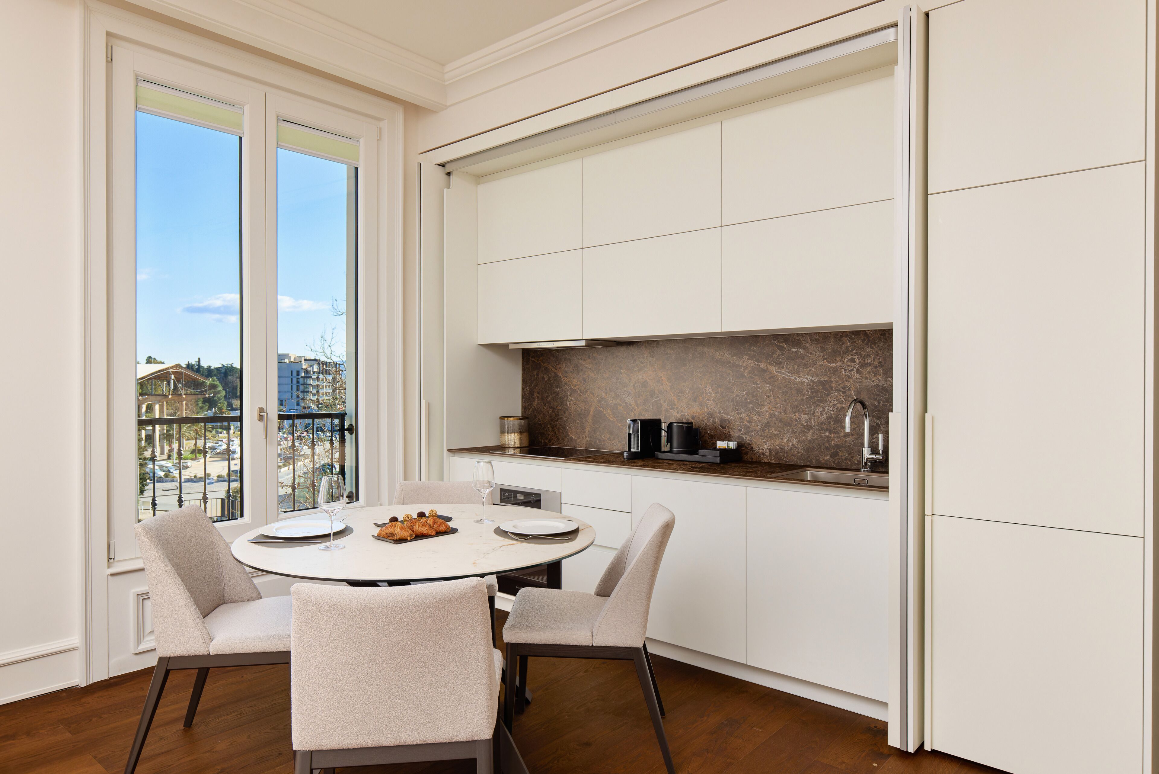 Una cocina moderna con armarios blancos, una mesa redonda para comer y vistas de la ciudad a través de amplios ventanales.