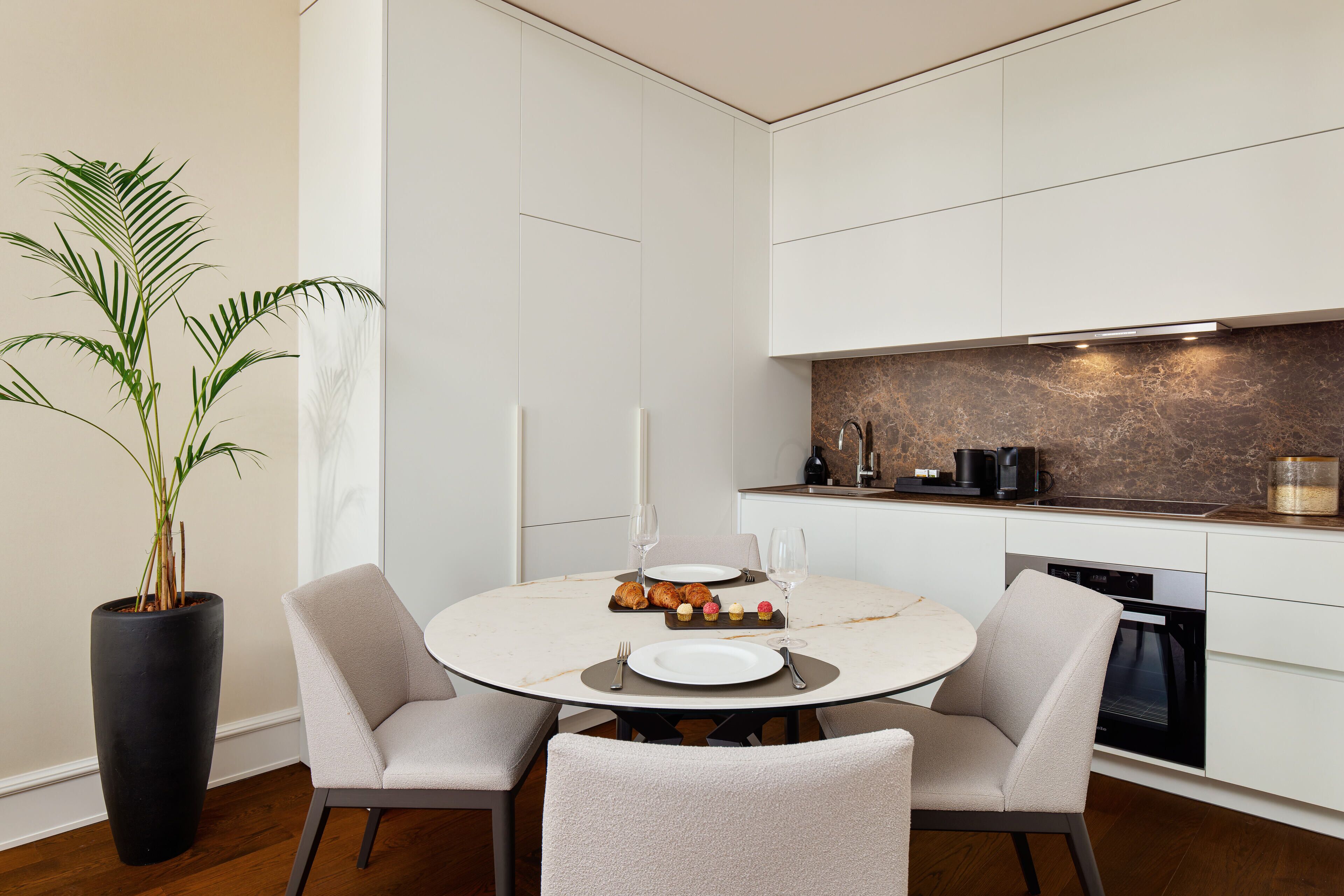 A modern kitchen with white cabinetry, a marble backsplash, and a dining area with a round table and chairs.