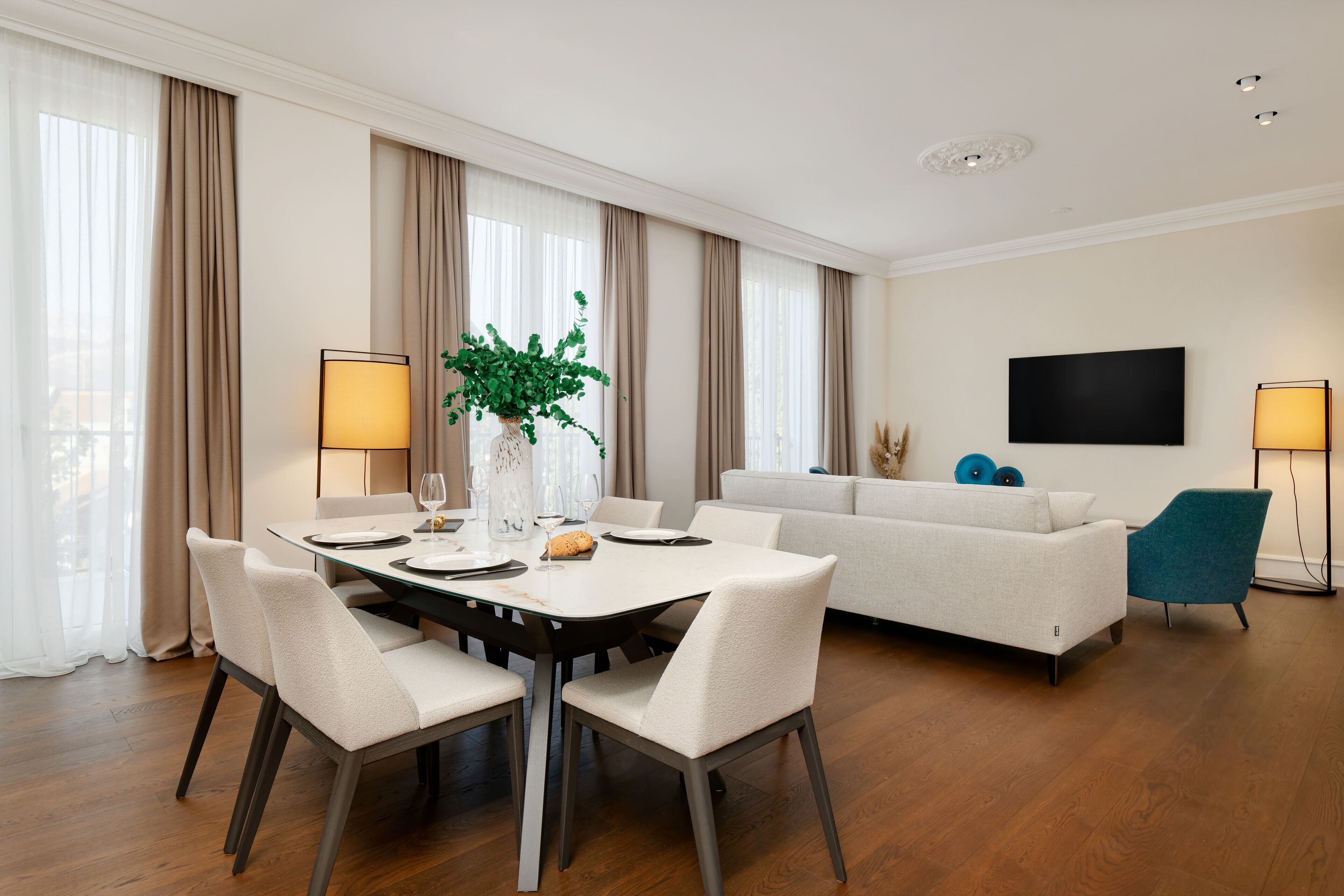 A modern living room with a dining area, a sofa, a TV, and a plant.