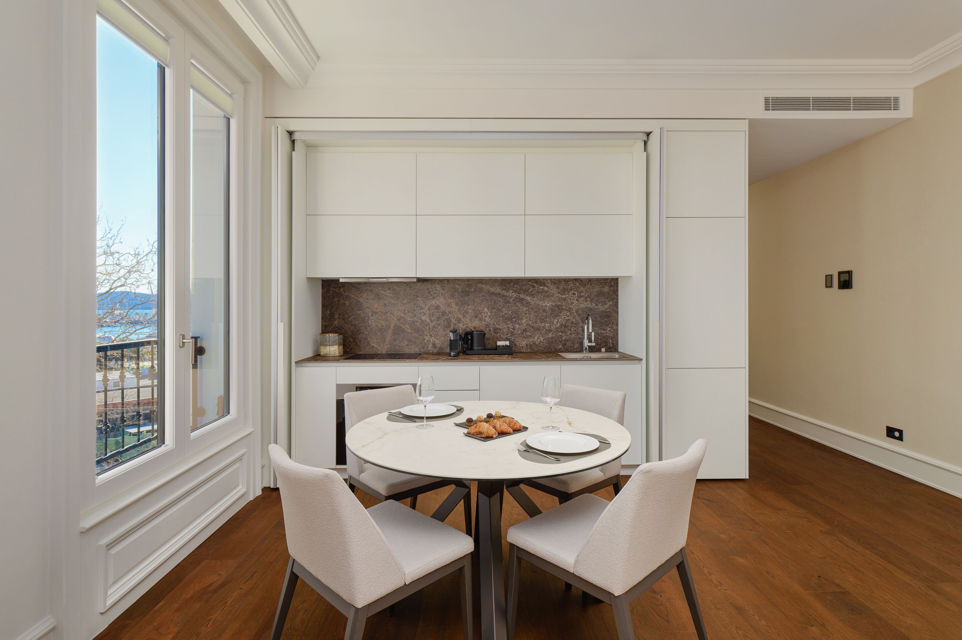 Un espace repas moderne avec une table ronde, quatre chaises et une vue sur un balcon.