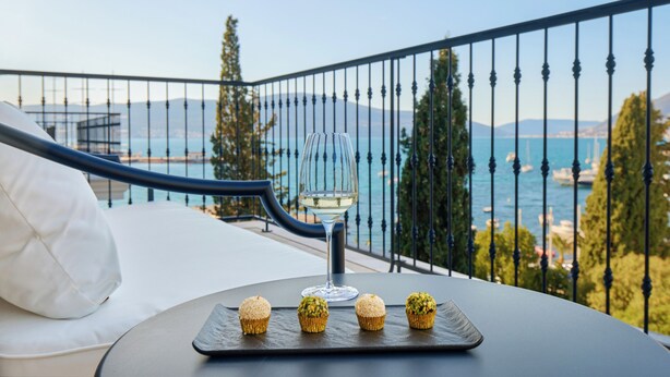 Balkon med havudsigt, et glas hvidvin og tre muffins på et fad.