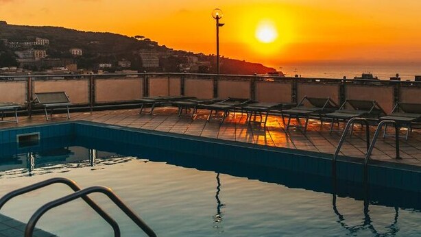 Una piscina en la azotea con sillones de descanso y vistas al atardecer.