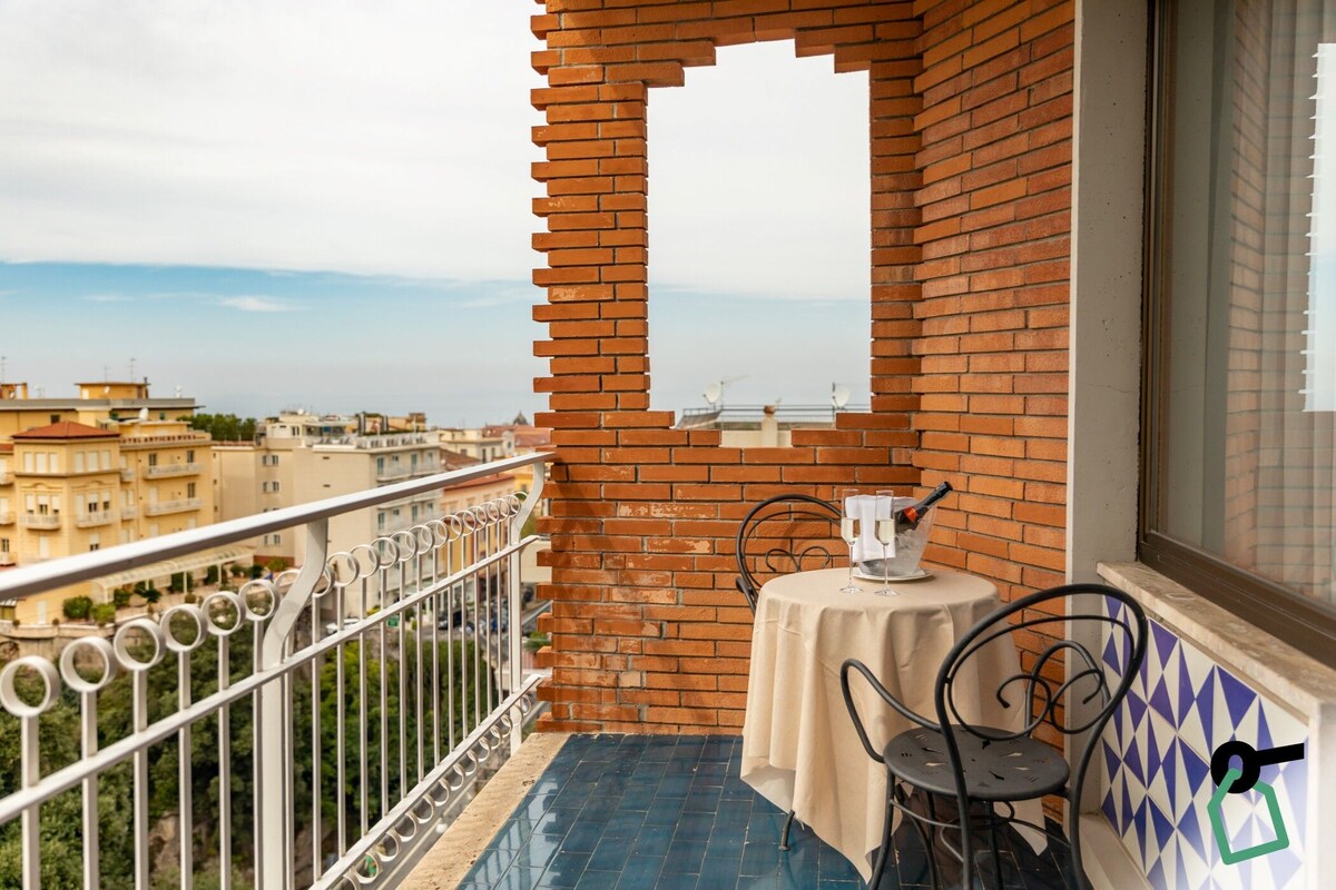 Een balkon met een tafel en stoelen, een bakstenen muur en een uitzicht op gebouwen in de verte.