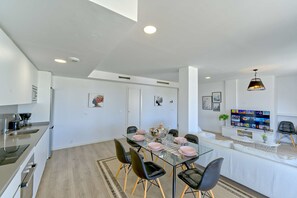 A modern kitchen with a dining area, a TV, and a ceiling light fixture.