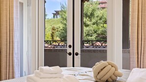 A hotel room with a bed, a set of towels, and a view through a door to a balcony with a railing.