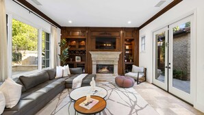 A spacious living room with a fireplace, a sectional sofa, a round coffee table, and a large window offering a view of the outdoors.