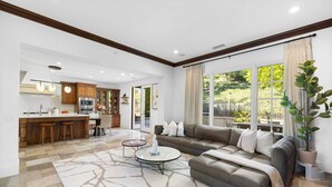 A spacious living area with a sofa, coffee table, and a view of the garden through large windows.