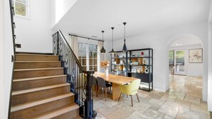 A spacious kitchen with a wooden staircase, a dining area with a table and chairs, and a bookshelf.