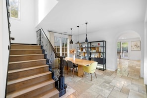 Una cocina amplia con una escalera de madera, un comedor con mesa y sillas, y una estantería.