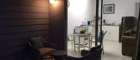 Uma área de pátio com mesa e cadeiras, uma pequena mesa redonda e uma porta de vidro deslizante que dá para uma cozinha e sala de estar.