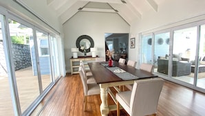 A spacious dining area with a long wooden table, cushioned chairs, and a large window offering a view of the outdoors.