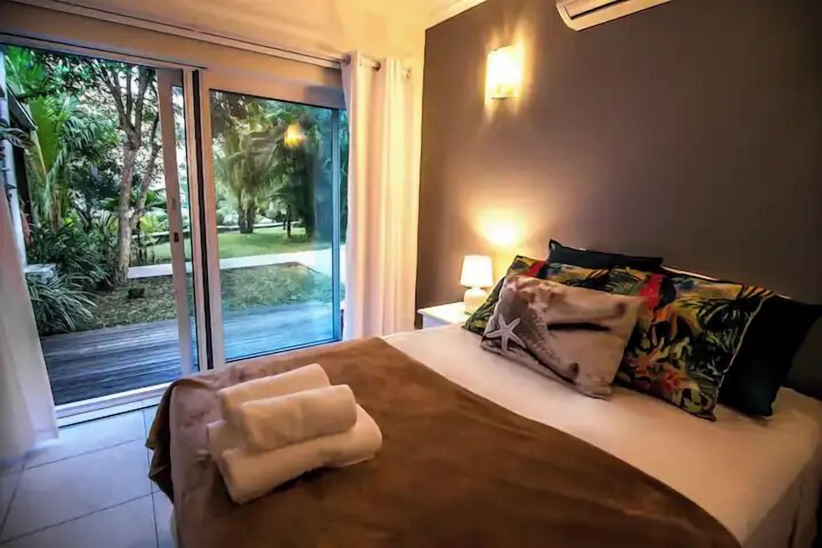 A hotel room with a bed, a nightstand, a lamp, and a view of a garden through a sliding door.