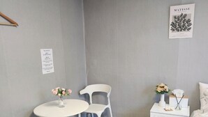 Une petite chambre à coucher, bien rangée, avec un lit simple, une table de chevet avec une lampe, une chaise, une petite table ronde ornée d’un vase de fleurs et une œuvre d’art encadrée accrochée au mur.