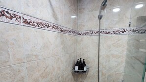 Un espace douche doté d’une porte en verre, d’un pommeau de douche et d’une étagère pour les articles de toilette.